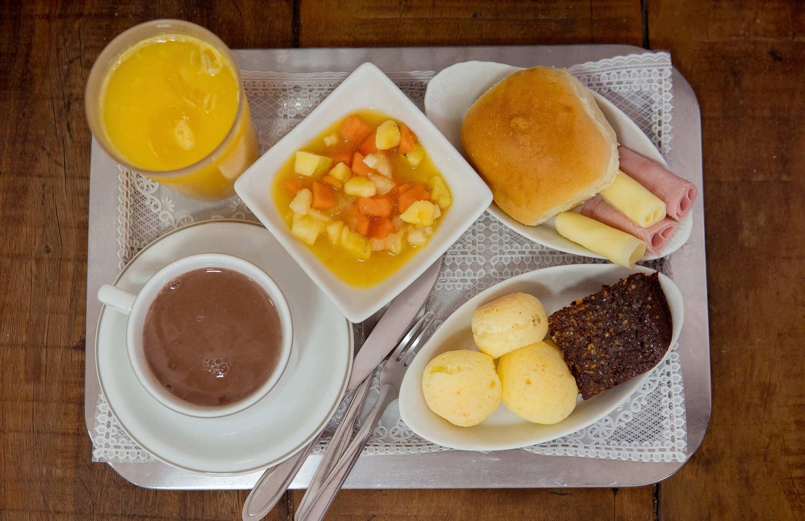 Café da manhã com bebida quente, suco, frutas, sanduíche e pães de queijo